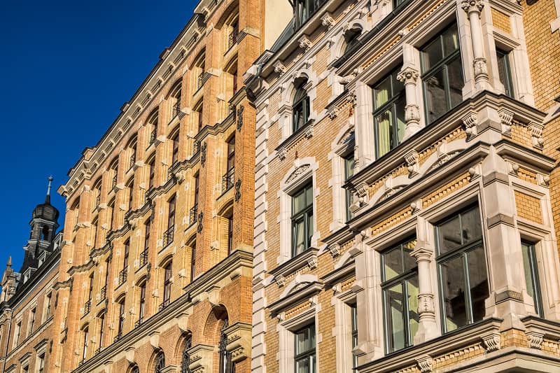 Fassade eines Altbaus mit verzierten Sandsteinelementen und mehreren Fenstern unter blauem Himmel